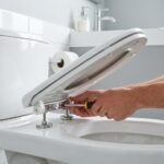 Close-up of a toilet seat being tightened with a screwdriver to stop it from sliding